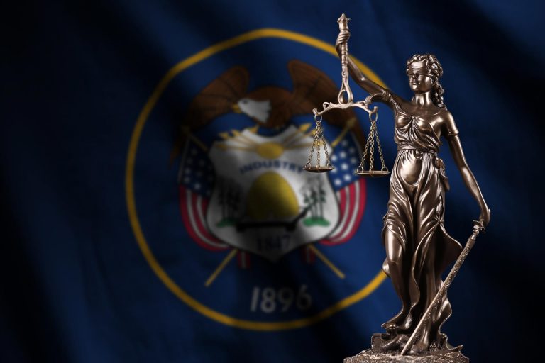 Utah US state flag with statue of lady justice and judicial scales in dark room.