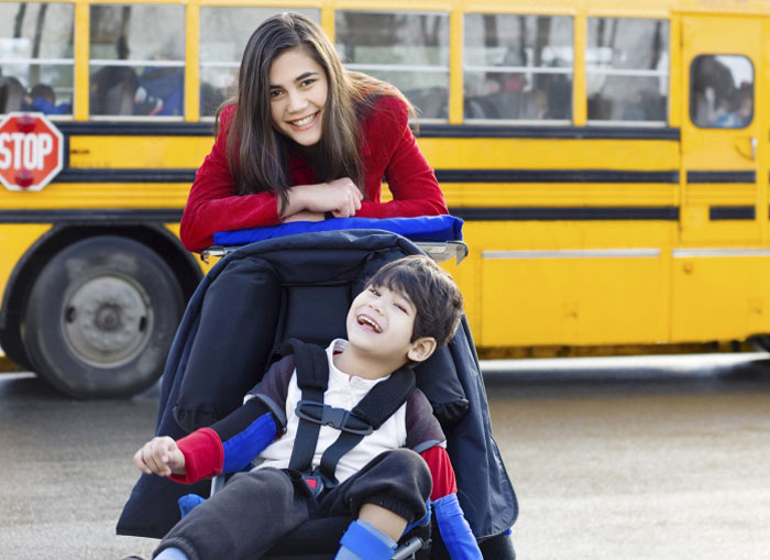 The caretaker woman and the child with disability in front of the school bus