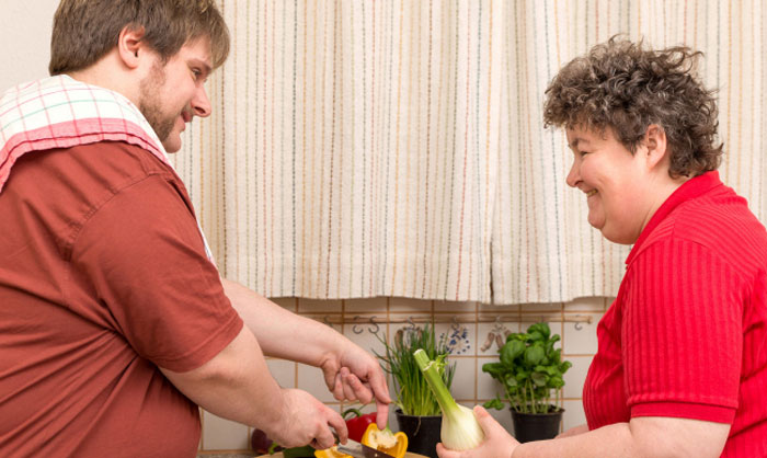 The gentleman is helping a woman with disability in the kitchen