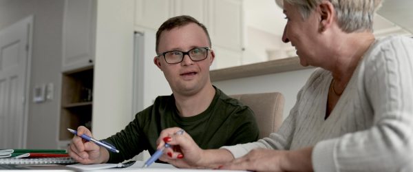 Young man with down syndrome at the kitchen table with senior woman.