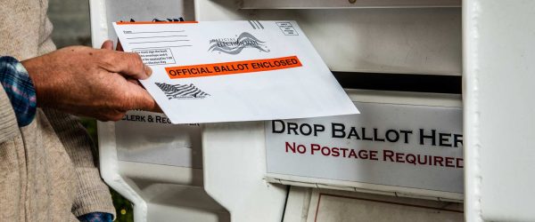 Man dropping voting ballot into a mail box.